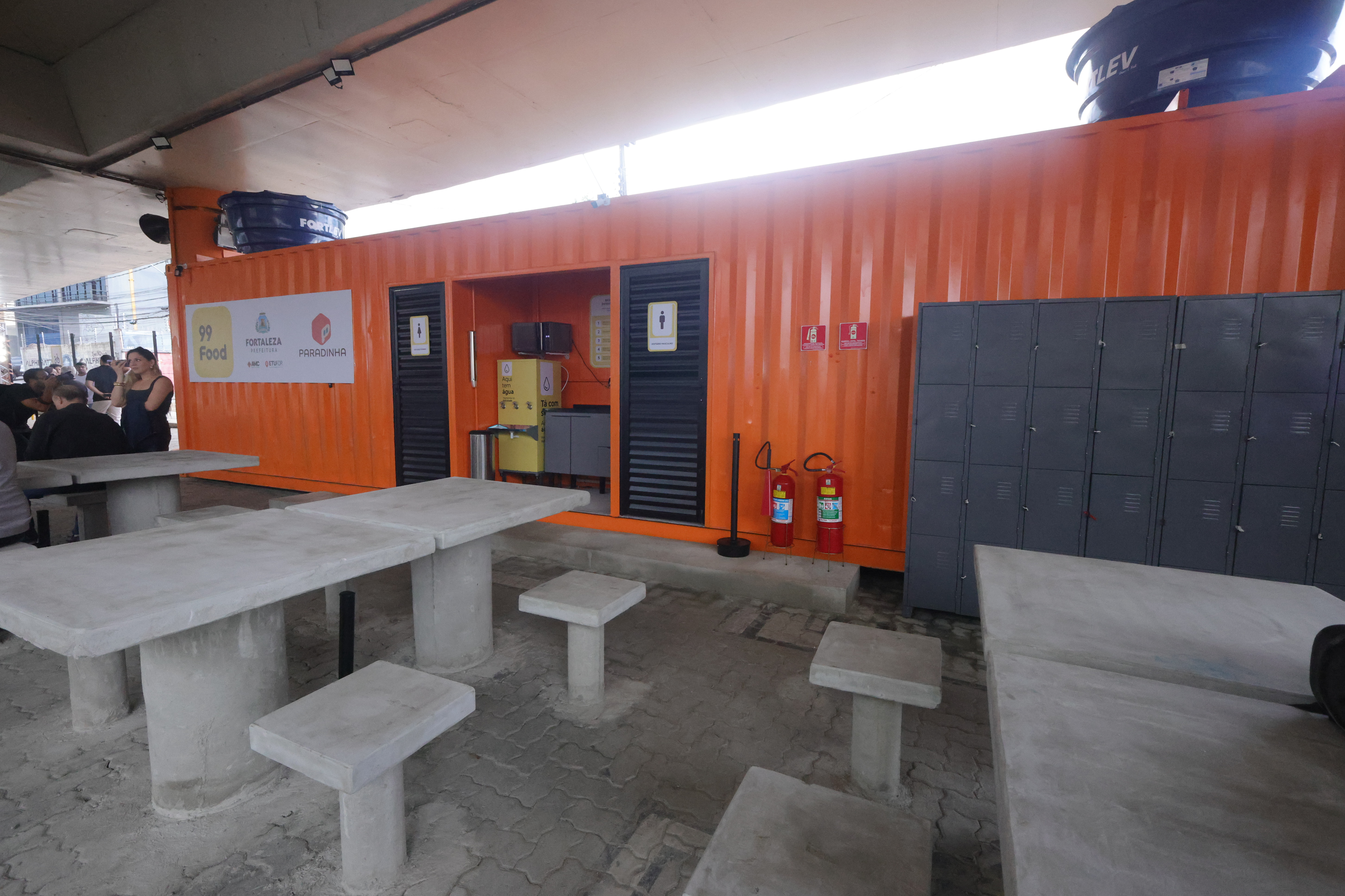 imagem interna da paradinha mostrando mesas, bancos e um conteiner 